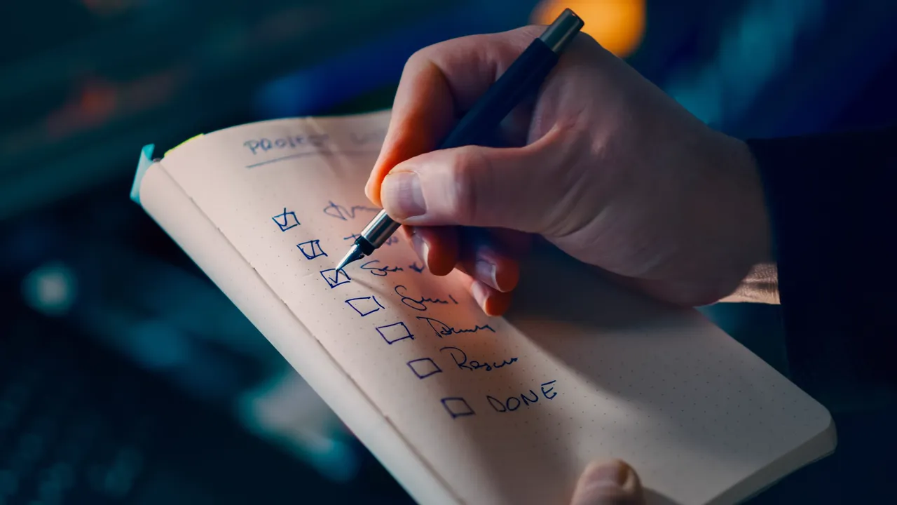 A hand ticking items off a handwritten checklist in a notebook