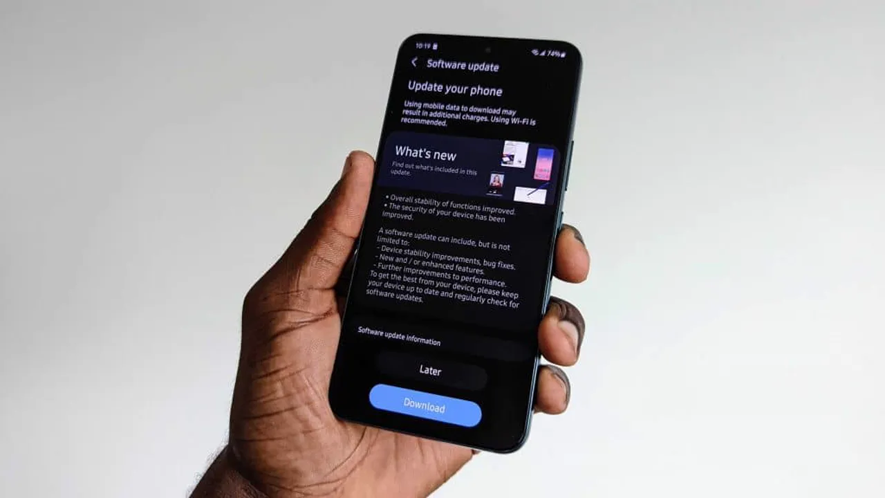 A hand holding a phone showing a software update screen with a download button