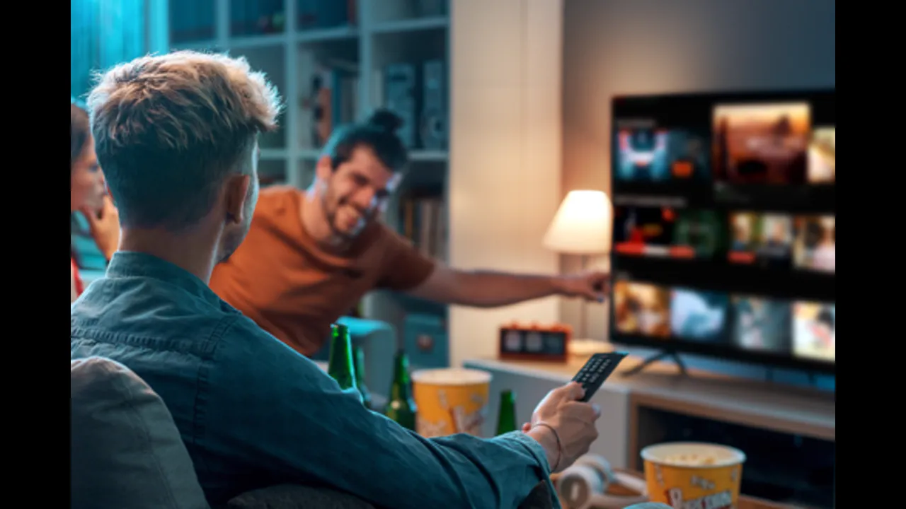 Friends with popcorn and a remote watching a television showing a streaming catalogue